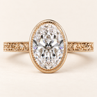 Oval cut lab grown diamond engagement ring with a full milgrain-detailed bezel, ornate filigree shoulders and polished yellow gold band.