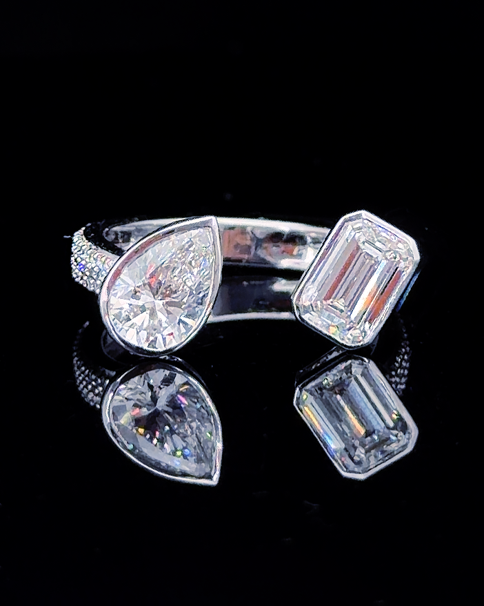 Main: White gold pear and emerald toi et moi ring with lab grown diamonds and pave shoulders on black
Detail: Close-up of pear and emerald-cut lab grown diamonds in contrasting white gold bezel settings
Side: White gold open toi et moi ring with pear and emerald lab grown diamonds and pave shoulders
