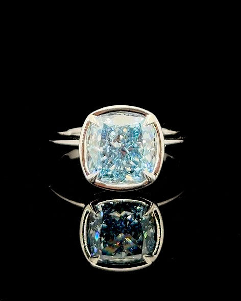 Main: White gold 5.08ct blue cushion solitaire ring with lab grown diamond centre on black
Detail: Close-up of 5.08ct blue cushion lab grown diamond in a four-prong white gold setting
Side: White gold solitaire ring with sculpted basket profile and blue cushion lab grown diamond