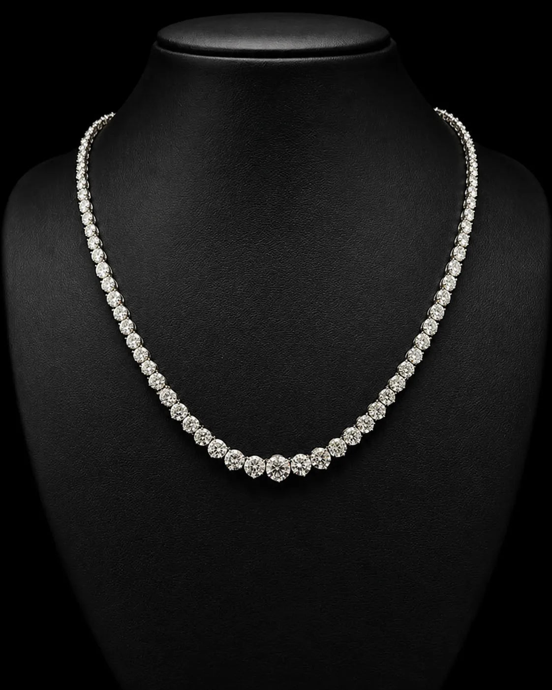 A sparkling diamond tennis necklace displayed on a black jewelry bust against a black background.