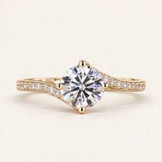 Round cut lab grown diamond bypass engagement ring in yellow gold with four-prong center, asymmetrical pavé shoulders and sweeping twist band.