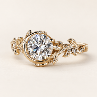 Round cut lab grown diamond engagement ring with sculptural partial bezel swirl, botanical leaf-and-vine shoulders and tiny diamond accents in polished yellow gold.