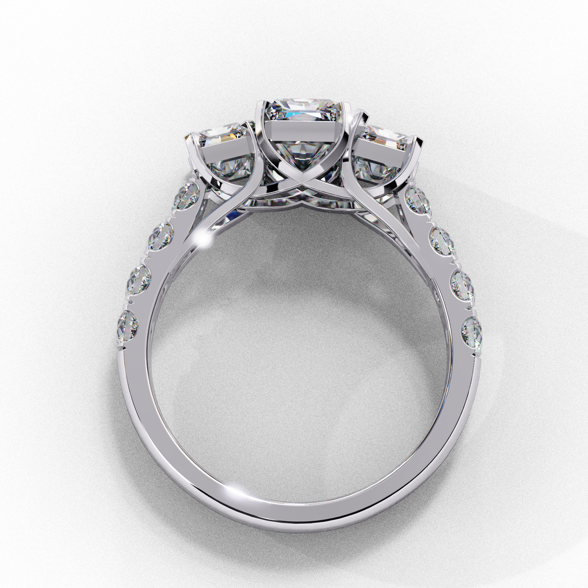 Side profile view of a white gold radiant cut three-stone diamond engagement ring with an open basket setting.