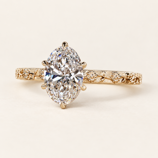 Oval cut lab grown diamond engagement ring with six sculpted claw prongs, floral and leaf engraved yellow gold shoulders and polished band.