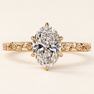 Oval cut lab grown diamond engagement ring with six sculpted claw prongs, floral and leaf engraved yellow gold shoulders and polished band.
