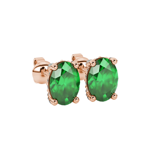 Close-up, oval cut emerald green gemstone earrings, rose gold pavé basket.