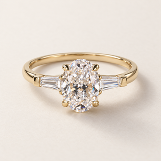 Oval lab grown diamond three-stone engagement ring in yellow gold with tapered baguette side diamonds and polished band