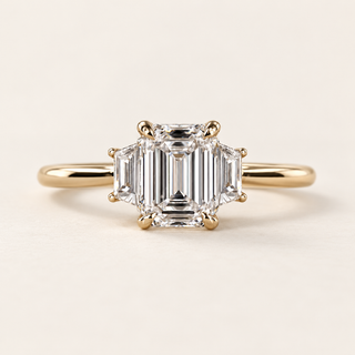 Emerald cut lab grown diamond three-stone engagement ring in yellow gold with trapezoid side diamonds, four center claws and a plain band