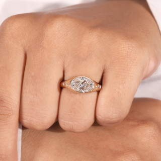 Yellow gold oval lab grown diamond men's signet ring with partial bezel setting and flush-set shoulder diamonds.