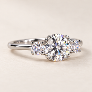 Round cut lab grown diamond three-stone engagement ring in white gold with two round brilliant side diamonds, decorative prong setting and polished band.