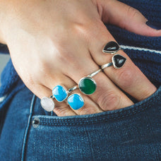 Close-up of a hand wearing multiple rings with heart and gemstone designs, against a blue denim background.