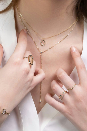 Close-up of a person wearing gold jewelry including a necklace, rings, and bracelet on a white background.