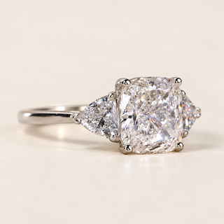 Cushion cut lab grown diamond three-stone engagement ring with 1.50 ct center diamond, two trillion cut side diamonds and polished yellow gold band.