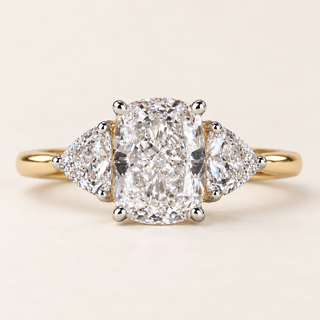 Cushion cut lab grown diamond three-stone engagement ring with 1.50 ct center diamond, two trillion cut side diamonds and polished yellow gold band.