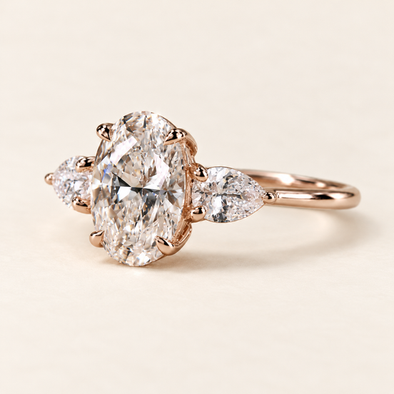 Oval cut lab grown diamond three-stone engagement ring in rose gold with outward-pointing pear side stones and four-prong oval center