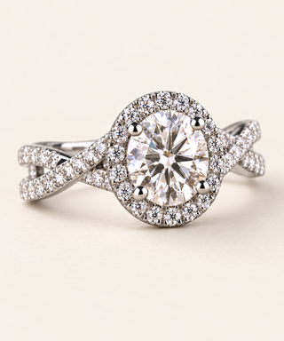 Round lab grown diamond crossover engagement ring in white gold with four-prong center, pavé halo and twisting diamond shoulders
