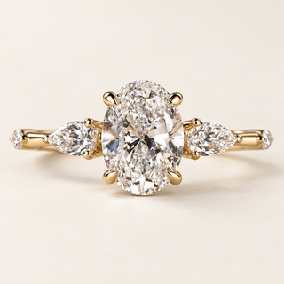 Oval cut lab grown diamond three-stone engagement ring in yellow gold with pear side diamonds, spaced round accents and polished shank