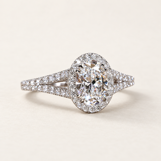 Oval cut lab grown diamond halo engagement ring in white gold with round diamond halo, pavé split shank and open triangular shoulders.