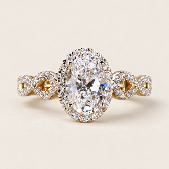 Oval cut lab grown diamond halo engagement ring with a 1.50 ct center, pavé halo and twisted diamond crossover shoulders in yellow gold with white-tone prongs.