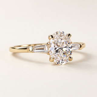 Oval lab grown diamond three-stone engagement ring in yellow gold with tapered baguette side diamonds and polished band