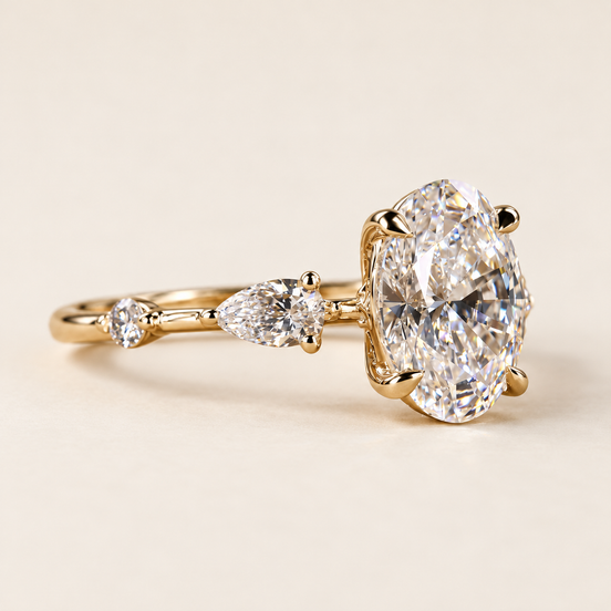Oval cut lab grown diamond three-stone engagement ring in yellow gold with pear side diamonds, spaced round accents and polished shank