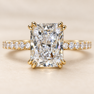 Radiant cut lab grown diamond hidden halo engagement ring in yellow gold with double claw corner prongs, pavé diamond shoulders and polished band.