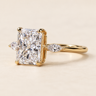 Radiant cut lab grown diamond three-stone engagement ring in yellow gold with two marquise side diamonds and four-prong center setting.