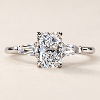 Radiant cut lab grown diamond three-stone engagement ring in white gold with four center prongs, tapered baguette side diamonds and polished shank.