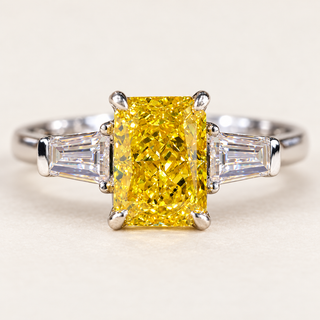 Vivid yellow radiant cut lab grown diamond three stone engagement ring in white gold with four-prong center and tapered baguette accents