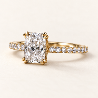 Radiant cut lab grown diamond hidden halo engagement ring in yellow gold with double claw corner prongs, pavé diamond shoulders and polished band.