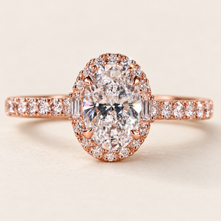 Oval cut lab grown diamond halo engagement ring in rose gold with two baguette diamonds, round brilliant halo and pavé diamond shoulders.