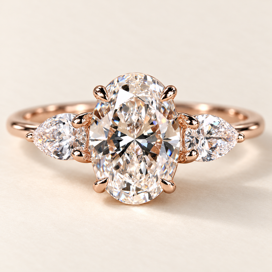 Oval cut lab grown diamond three-stone engagement ring in rose gold with outward-pointing pear side stones and four-prong oval center
