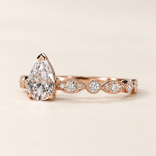 Pear cut lab grown diamond vintage engagement ring in rose gold with protective V-prong, leaf-inspired openwork shoulders and round diamond accents.