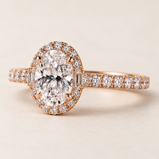 Oval cut lab grown diamond halo engagement ring in rose gold with two baguette diamonds, round brilliant halo and pavé diamond shoulders.