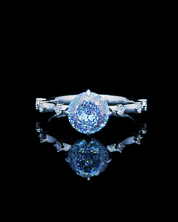 Main: White gold 1.71ct blue round ring with spaced lab grown diamond accents on black
Detail: Close-up of 1.71ct blue round lab grown diamond held in a four-prong white gold setting
Side: White gold blue round ring with six individually set lab grown diamond shoulder accents