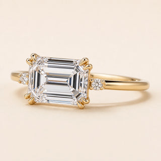Emerald cut Lab Grown Diamond east-west engagement ring in yellow gold with a double-claw four-prong cathedral setting and hidden side diamonds.