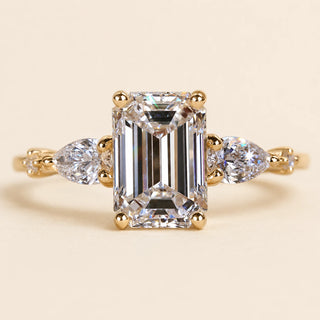 Emerald cut Lab Grown Diamond three stone engagement ring in yellow gold with pear side diamonds and four-prong basket setting.
