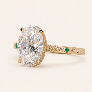 Oval Lab Grown Diamond vintage engagement ring in yellow gold with a hidden halo, engraved shank and emerald side accents.