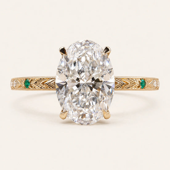 Oval Lab Grown Diamond vintage engagement ring in yellow gold with a hidden halo, engraved shank and emerald side accents.