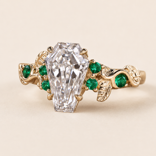 Coffin cut lab grown diamond engagement ring in yellow gold with round green gemstone accents and leaf-and-vine shoulders