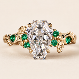 Coffin cut lab grown diamond engagement ring in yellow gold with round green gemstone accents and leaf-and-vine shoulders