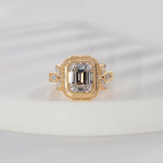 Emerald cut lab grown diamond vintage engagement ring in yellow gold with bezel center, marquise side diamonds and engraved shoulders