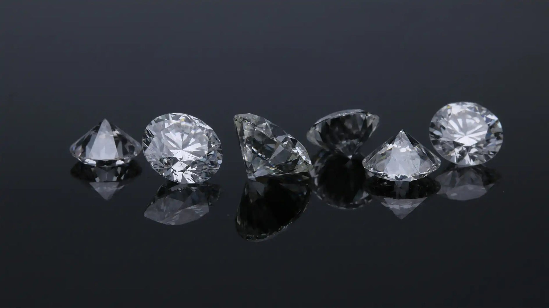Set of diamonds of various shapes and sizes on a reflective black surface