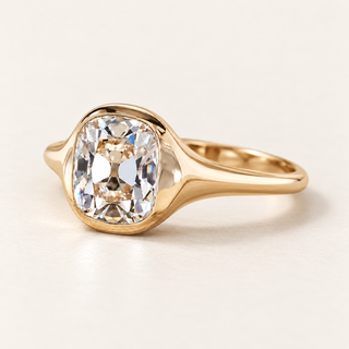Cushion old mine cut lab grown diamond bezel engagement ring in yellow gold with broad tapered shoulders and polished shank