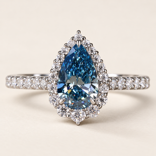 Blue pear cut lab grown diamond halo engagement ring in white gold with three center prongs, round diamond surround and pavé shoulders