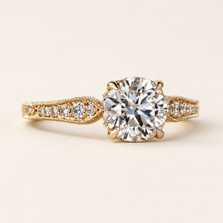 Round cut lab grown diamond engagement ring with six-claw center setting, round diamond-set leaf shoulders, milgrain edges and filigree detailing in yellow gold.