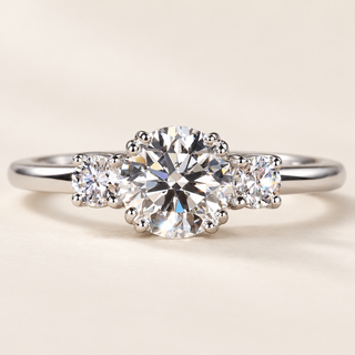 Round cut lab grown diamond three-stone engagement ring in white gold with two round brilliant side diamonds, decorative prong setting and polished band.