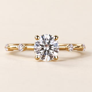Round lab grown diamond four-prong engagement ring in yellow gold with spaced round diamond accents and slim polished band