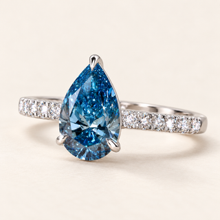 Blue pear cut lab grown diamond solitaire engagement ring in white gold with protective tip prong and diamond-set shoulders