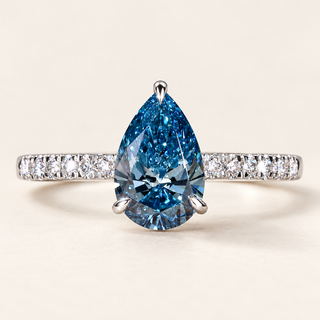 Blue pear cut lab grown diamond solitaire engagement ring in white gold with protective tip prong and diamond-set shoulders